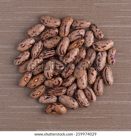 Top view of circle of pinto beans against brown vinyl background.