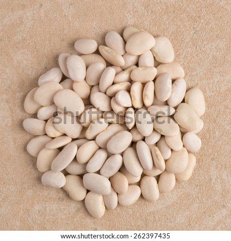 Top view of circle of white beans against beige vinyl background.