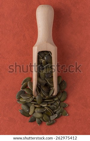 Top view of wooden scoop with pumpkin seeds against red vinyl background.