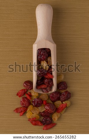 Top view of wooden scoop with mixed dried fruits against brown vinyl background.