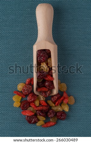 Top view of wooden scoop with mixed dried fruits against blue vinyl background.