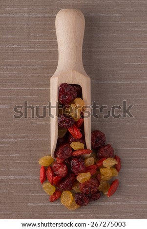Top view of wooden scoop with mixed dried fruits against beige vinyl background.
