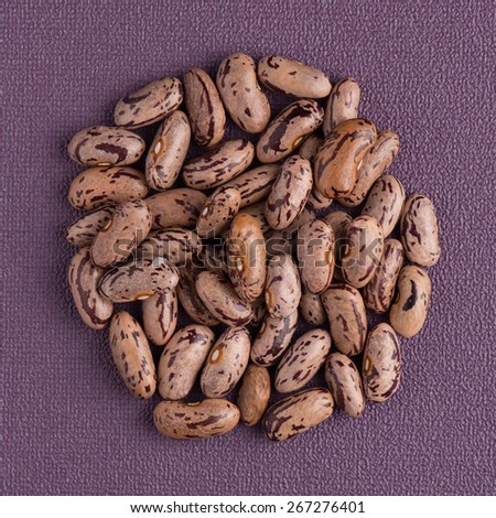 Top view of circle of pinto beans against purple vinyl background.