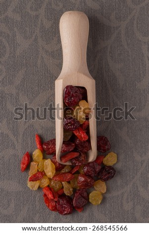 Top view of wooden scoop with mixed dried fruits against grey vinyl background.
