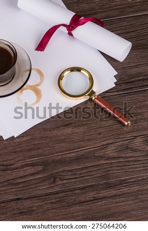 Coffee cup, paper sheets and detective magnifying glass on old Wooden table.