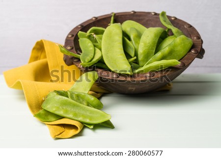 Snow peas on wooden bowl with green napkin on wooden table.