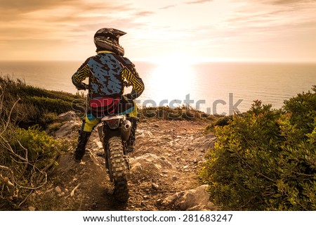 Enduro racer sitting on his motorcycle watching the sunset.