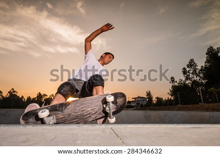 Skateboarder in a concrete pool at skatepark on a beautiful sunset.