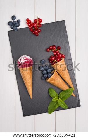Red fruits ice cream cone on wooden table.