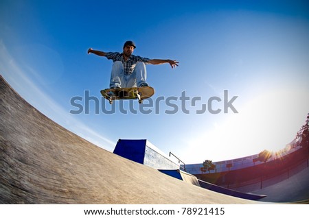 Skateboarder flying over a ramp on sunset at the local skate park.