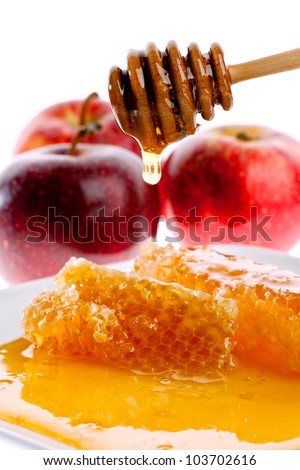 honey dripping off wand above dish with honeycomb, with fresh apples in background