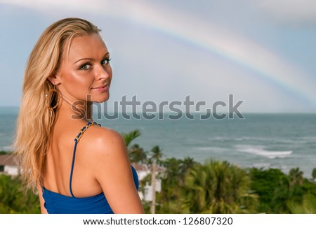 lovely blond female in blue dress against tropical island and ocean with rainbow
