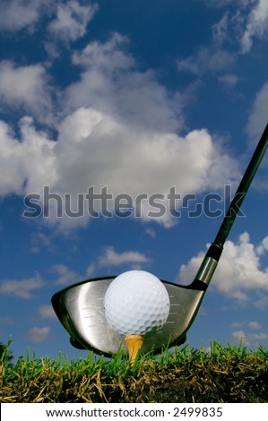 golf ball on tee with driver from ground level, with lots of blue sky and puffy clouds for copy