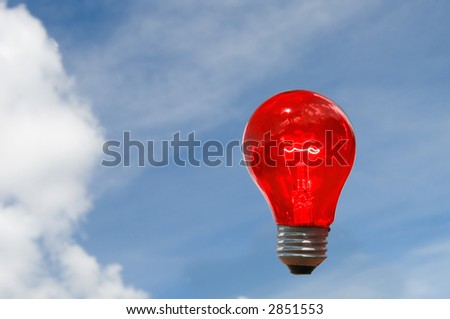 glowing clear red light bulb as stop against blue sky with puffy clouds