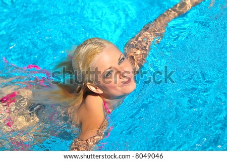 attractive blond female model in pink bikini swimming in pool