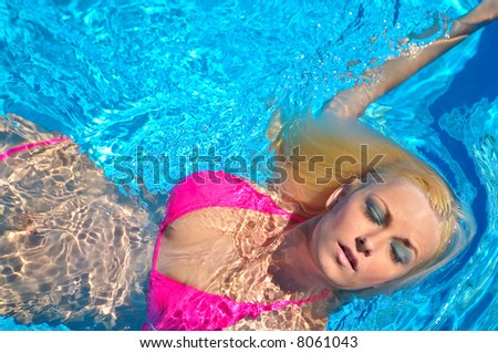 attractive blond female model in pink bikini swimming in pool