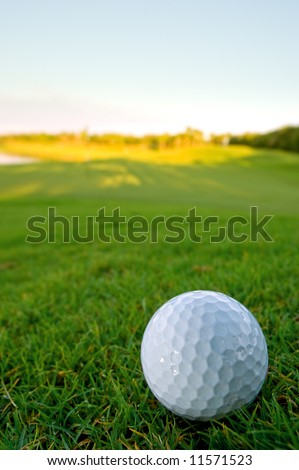 golf ball resting on bunker of lovely golf course with pale blue sky and shallow depth of field