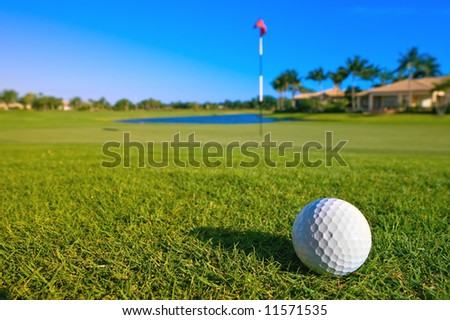 golf ball near green and pin of lovely tropical golf course with clear blue sky
