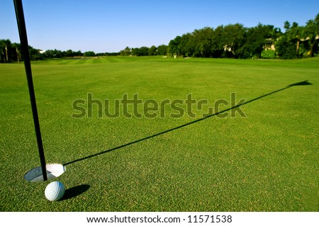 golf ball near hole and pin of lovely tropical golf course with clear blue sky