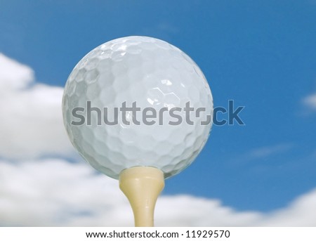golf ball on tee isolated against blue sky with puffy clouds