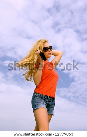 lovely blonde female model listening to portable radio against hazy blue sky