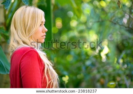 attractive blond model profile shot with red sweater at garden with background copy space out of focus