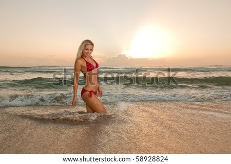 lovely blonde bikini model walks from atlantic ocean at beach at dawn
