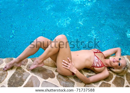 lovely blond female in bikini relaxing beside pool, with copy space
