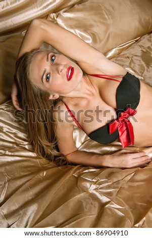 lovely brunette female lingerie model with red accents against gold satin linens