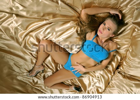 lovely brunette female lingerie model in blue lace top and bottom against gold satin linens