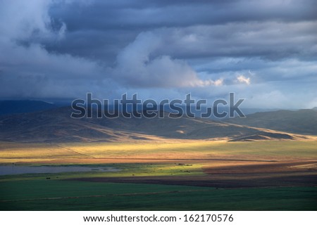 Storm sky and sun gaps on the fields and hills on the horizon