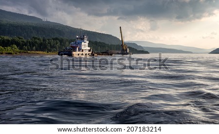 KRASNOYARSK REGION, RUSSIA - JULY 10, 2014: Tugboat named Hero Moskvin pulling a barge loaded with coal on the Yenisei River