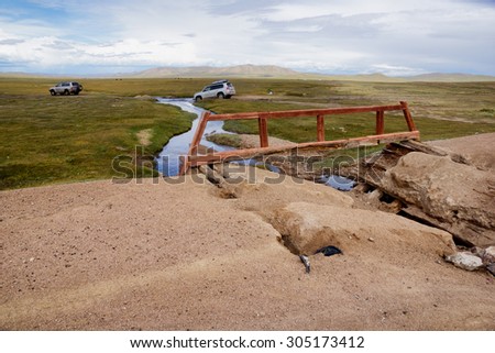 WESTERN MONGOLIA, MONGOLIA - AUG 26, 2012: Foreign tourists in cars go around the broken bridge over a small river.