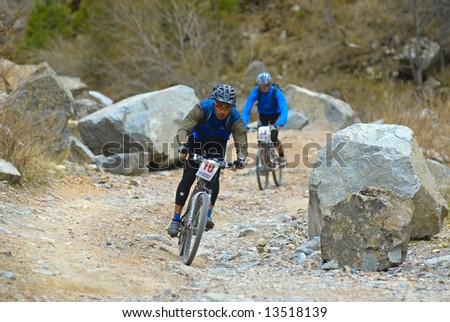 Two bikers downhill on old rural road in desert mountains