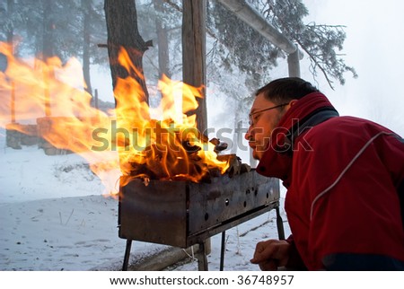 Man fanning the fire in the grill on winter forest