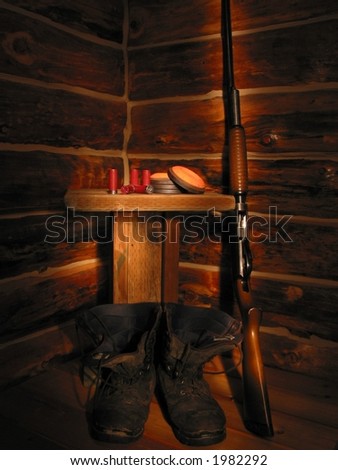 A portrait view of a shotgun standing in the corner of a log cabin beside a table and boots.