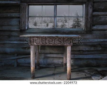 An old table sits in front of a window in an abandoned cabin in the winter.
