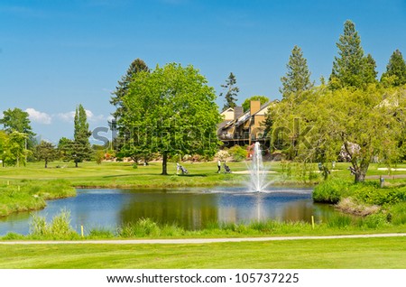 Golf place with gorgeous green, pond and row of houses on background.