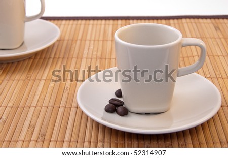 Two small cappuccino cups and coffee beans on bamboo mat. Shallow depth of field. Focus on the closest cup and coffee beans.