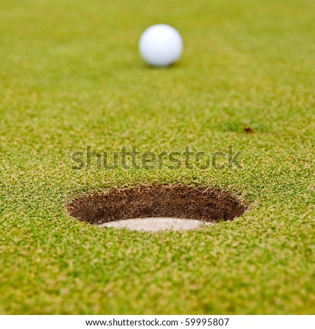 A hole over golf ball on green. Shallow depth of field. Focus on the hole.