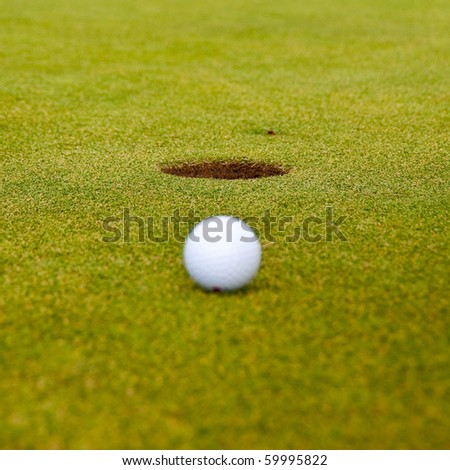 Golf ball on green with a hole. Shallow depth of field. Focus on the hole.