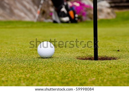 Golf ball on green with a hole. Shallow depth of field. Focus on the ball and the hole.