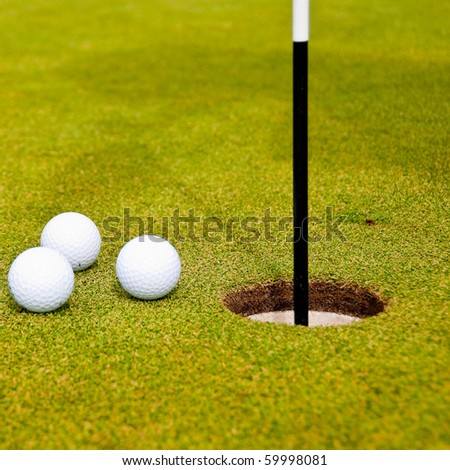 Three golf balls on green with a hole. Shallow depth of field. Focus on the hole and the closest balls.