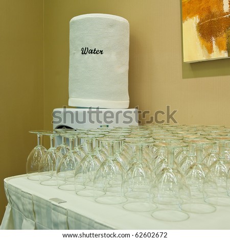 A water station and stack of glasses. Shallow depth of field. Focus on the water canteen.