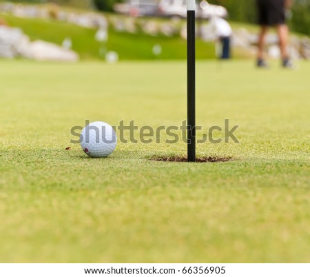 Golf ball on green with flag. Shallow depth of field. Focus on the ball and the hole.