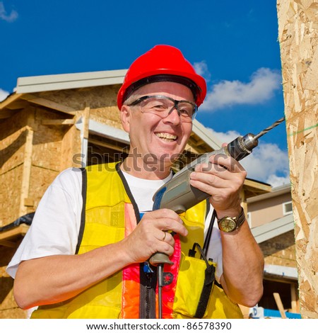 A man in a hard hat standing in front of an house holding a drill in his hand.