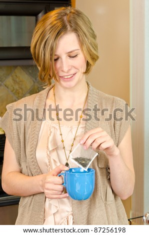 Portrait of a smiling female standing and making cap of tea in the kitchen