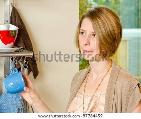 Portrait of a confused female standing and holding a cap in the kitchen
