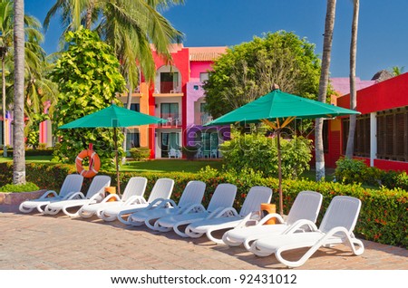 White resort pool chairs in row over beautiful garden and colorful buildings