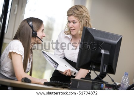 Two female employees discuss  work in an office.